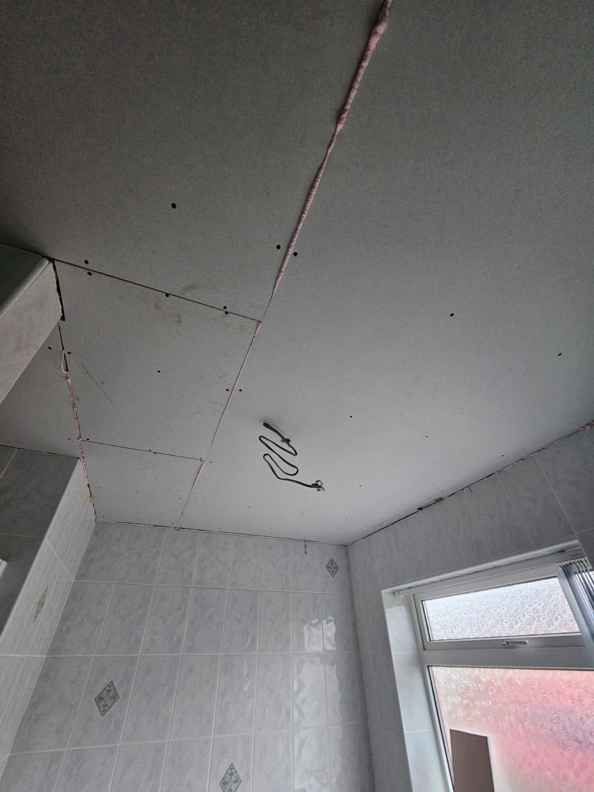 A bathroom ceiling freshly re-boarded with plasterboard above white tiles