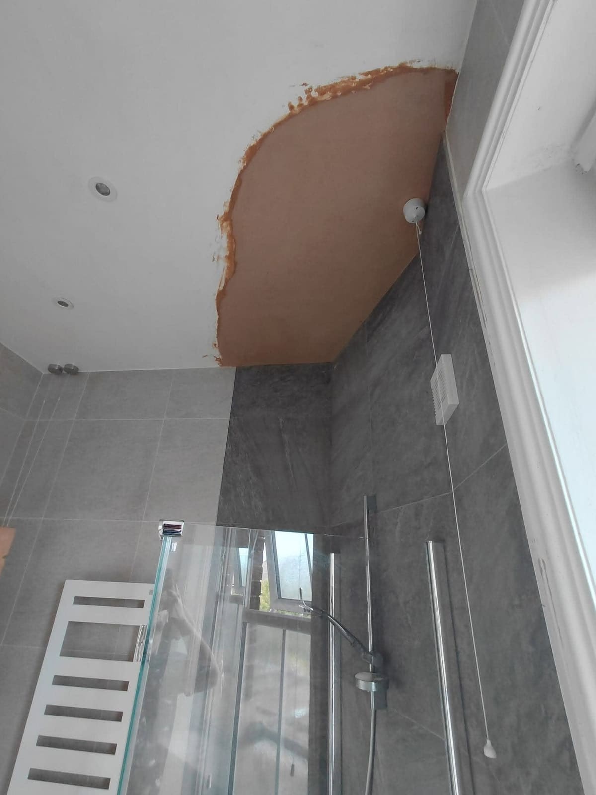 A freshly plastered patch on a bathroom ceiling above a tiled shower enclosure