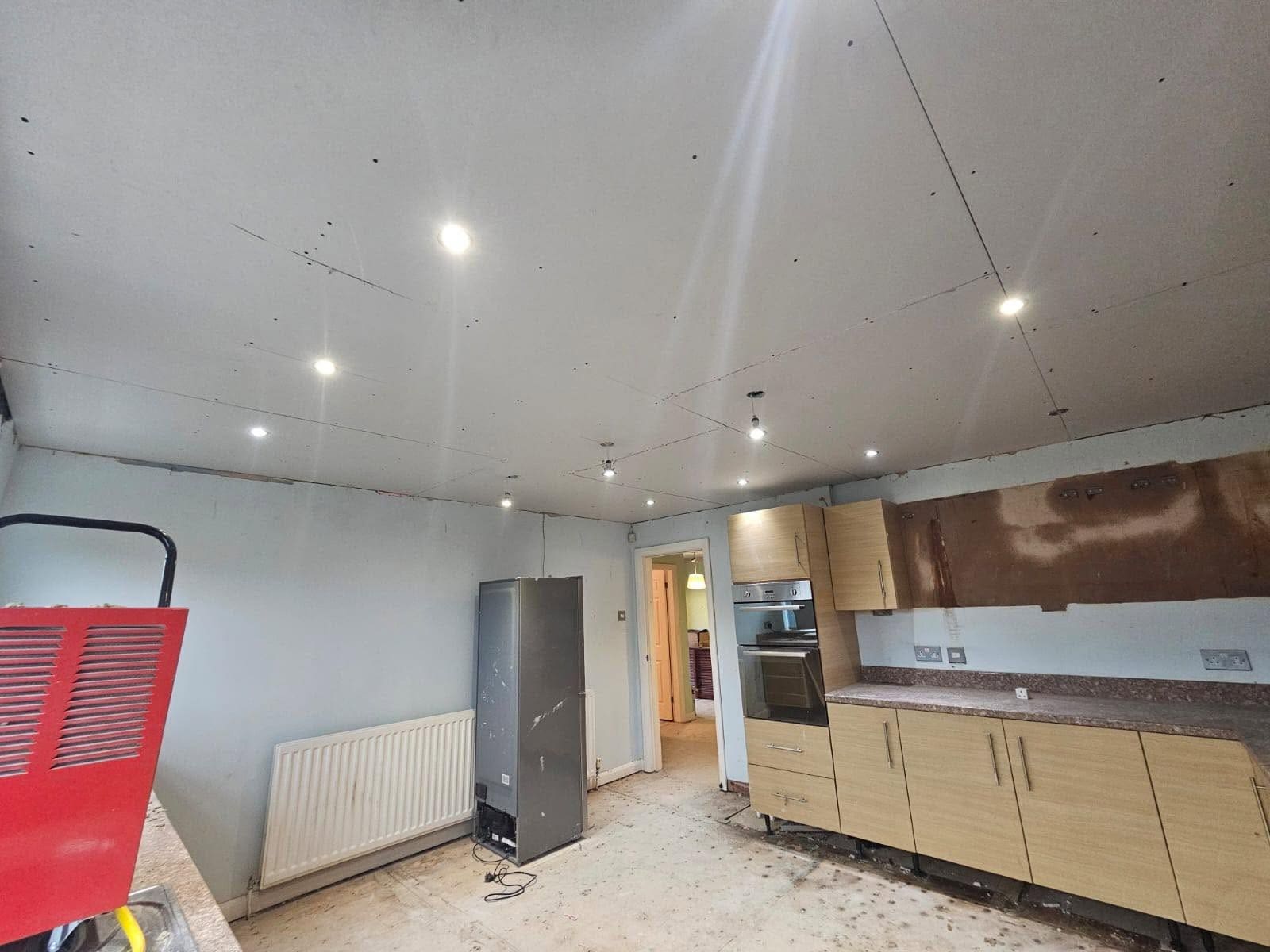 A kitchen ceiling freshly boarded with downlights cut in and a dehumidifier running