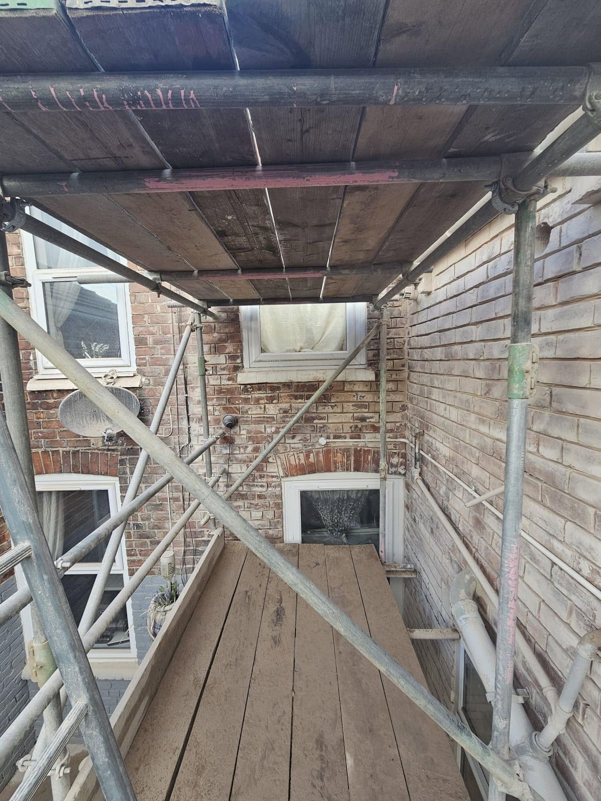Scaffold boards along the rear of a terraced house with the brickwork prepared for render