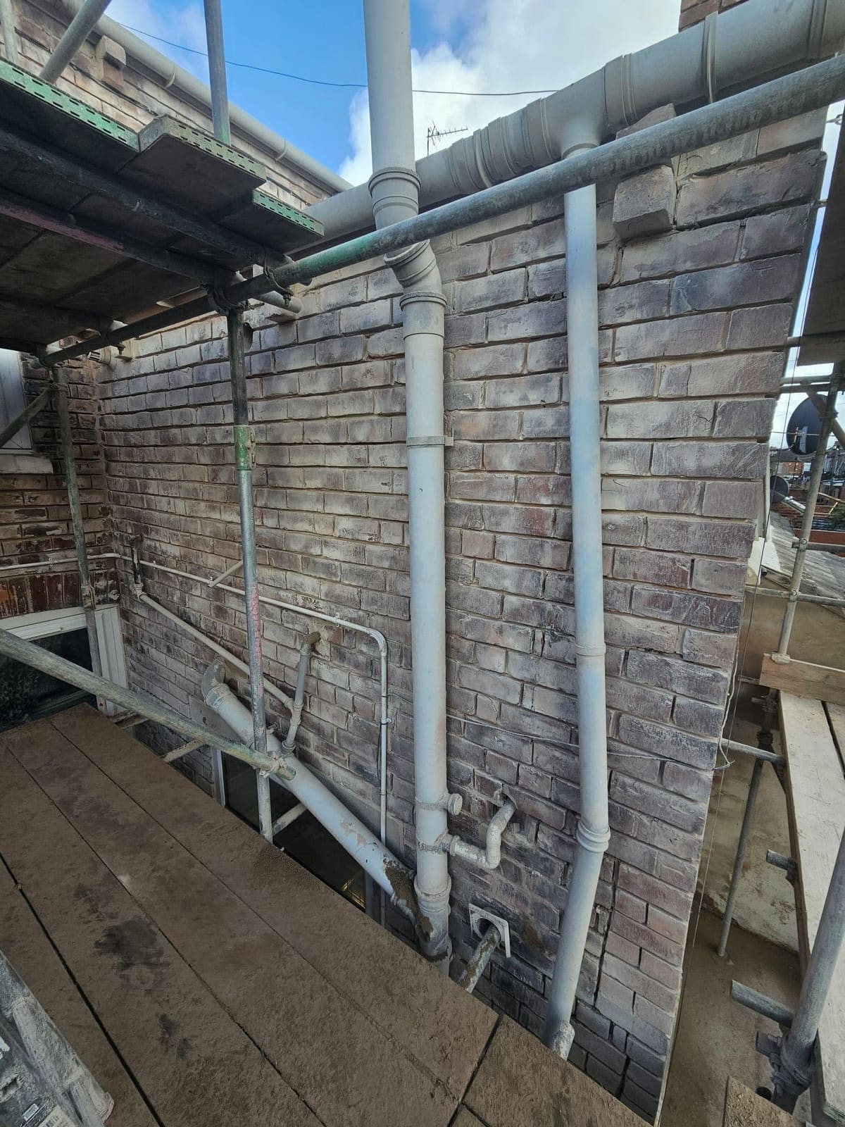 Downpipes and soil pipe against the prepared rear wall, seen from the scaffold