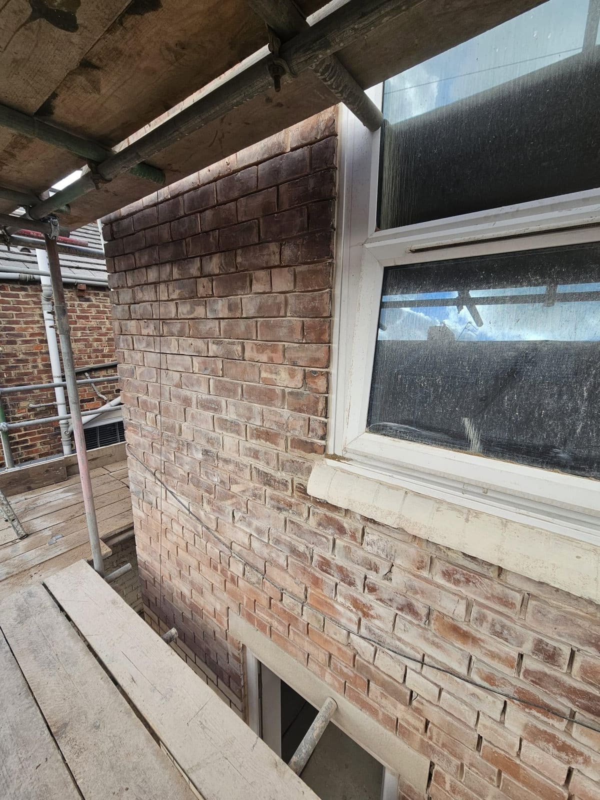 The brick wall of a rear extension seen from the scaffold, prepared for render around a first-floor window